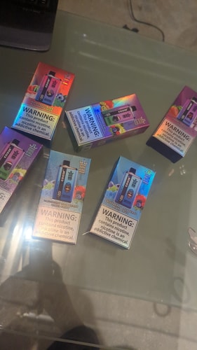 Several boxes of colorful disposable vape devices labeled "Bang King" are displayed on a glass surface. The packaging features various fruit flavor images and prominent nicotine addiction warnings.