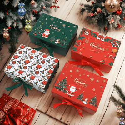 Cuatro cajas de regalo navideñas festivas (dos rojas, una verde y una blanca con estampado de flor de pascua), atadas con cintas y decoradas con Papá Noel y motivos navideños, dispuestas sobre un piso de madera debajo de ramas de pino y adornos colgantes.