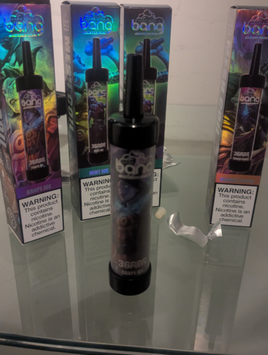 Een display met wegwerp-vape-pennen van het merk Bang in verschillende smaken, waaronder Grape Ice, Mint Ice en Mango Peach, elk voorzien van een nicotinewaarschuwing.